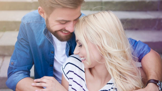 Pareja sonriente sentada abrazándose en unas escaleras, representando el tiempo libre o los días libres por pareja de hecho.